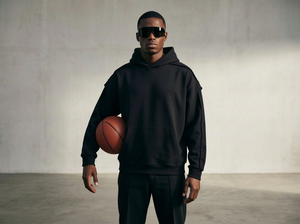 Man in black hoodie and sunglasses holding a basketball against a plain background